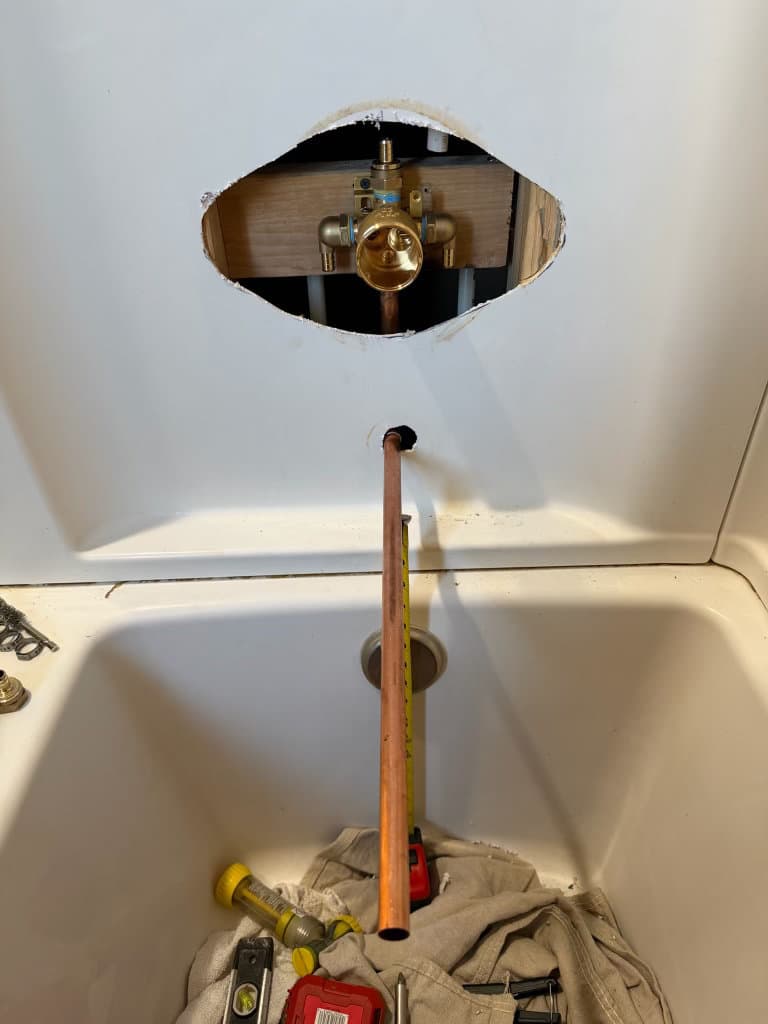 During: new brass shower valve body installed through access hole, copper tub spout pipe in place — Oopsie Daisy Plumbing